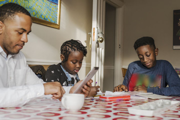 Dad on tablet with son and daughter doing homework