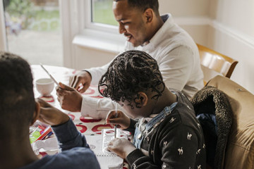 Dad on tablet with son and daughter doing homework